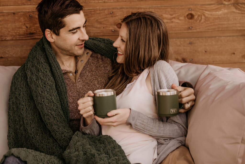 man and woman sit on couch with coffee during colorado airbnb engagement photos.