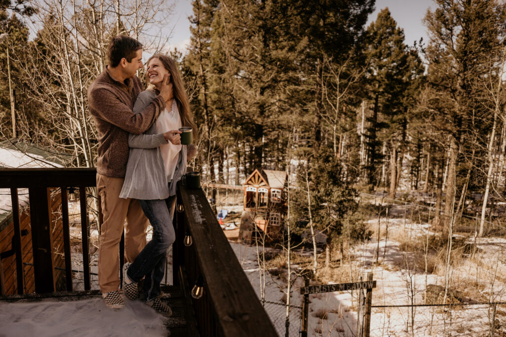 man and woman stand on porch of airbnb during colorado engagement photos.