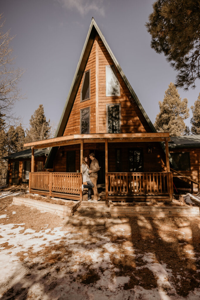 man and woman stand on porch of airbnb during colorado couples portraits.