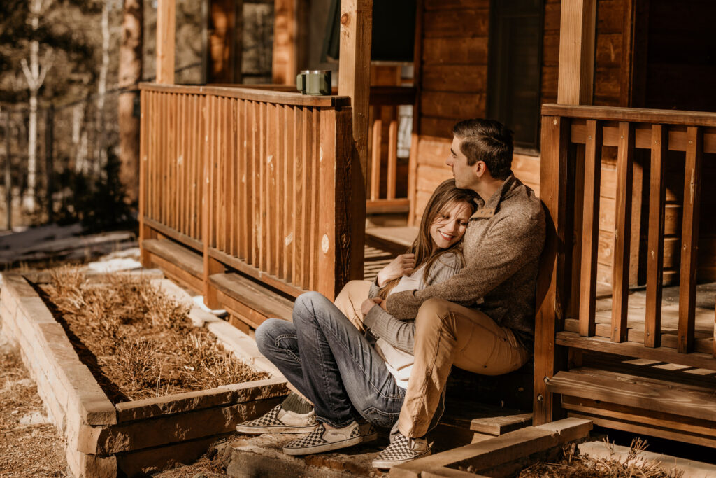 man and woman sit on porch of airbnb during colorado mountain engagement photos.