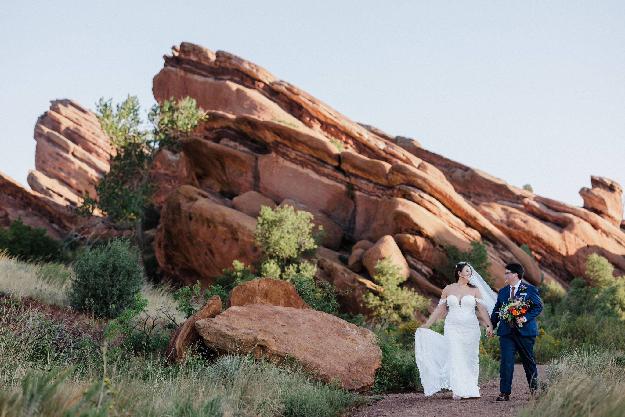 lgbtq+ couple holds hands as they walk through red rocks park and amphitheatre