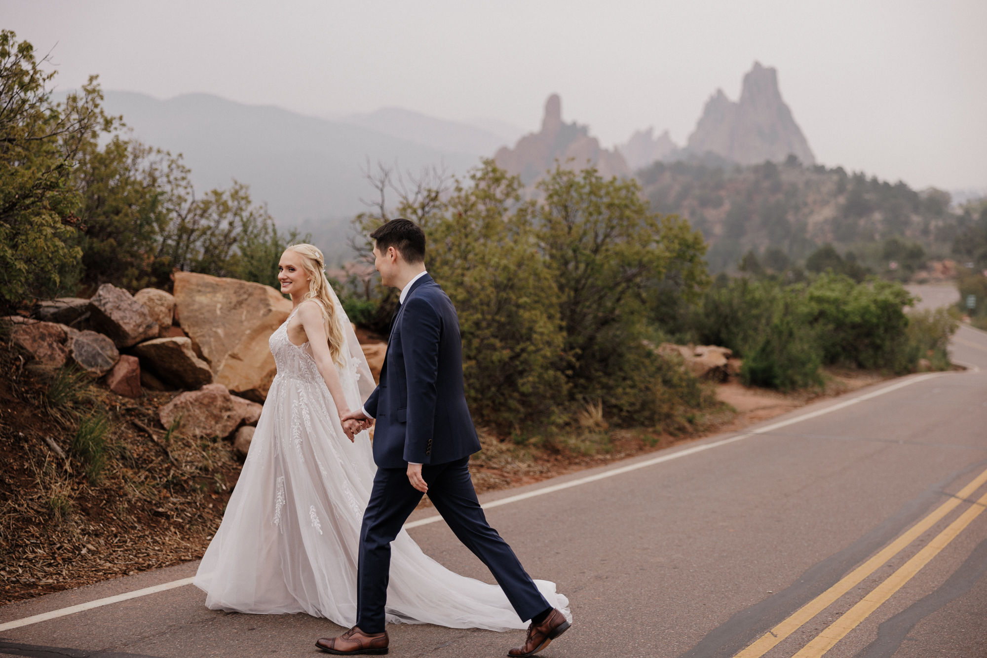 bride and groom walk across road at garden of the gods park during their colorado wedding day.