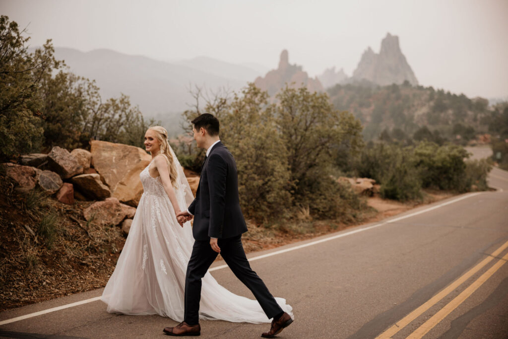 bride and groom walk across road at garden of the gods park during their colorado wedding day.