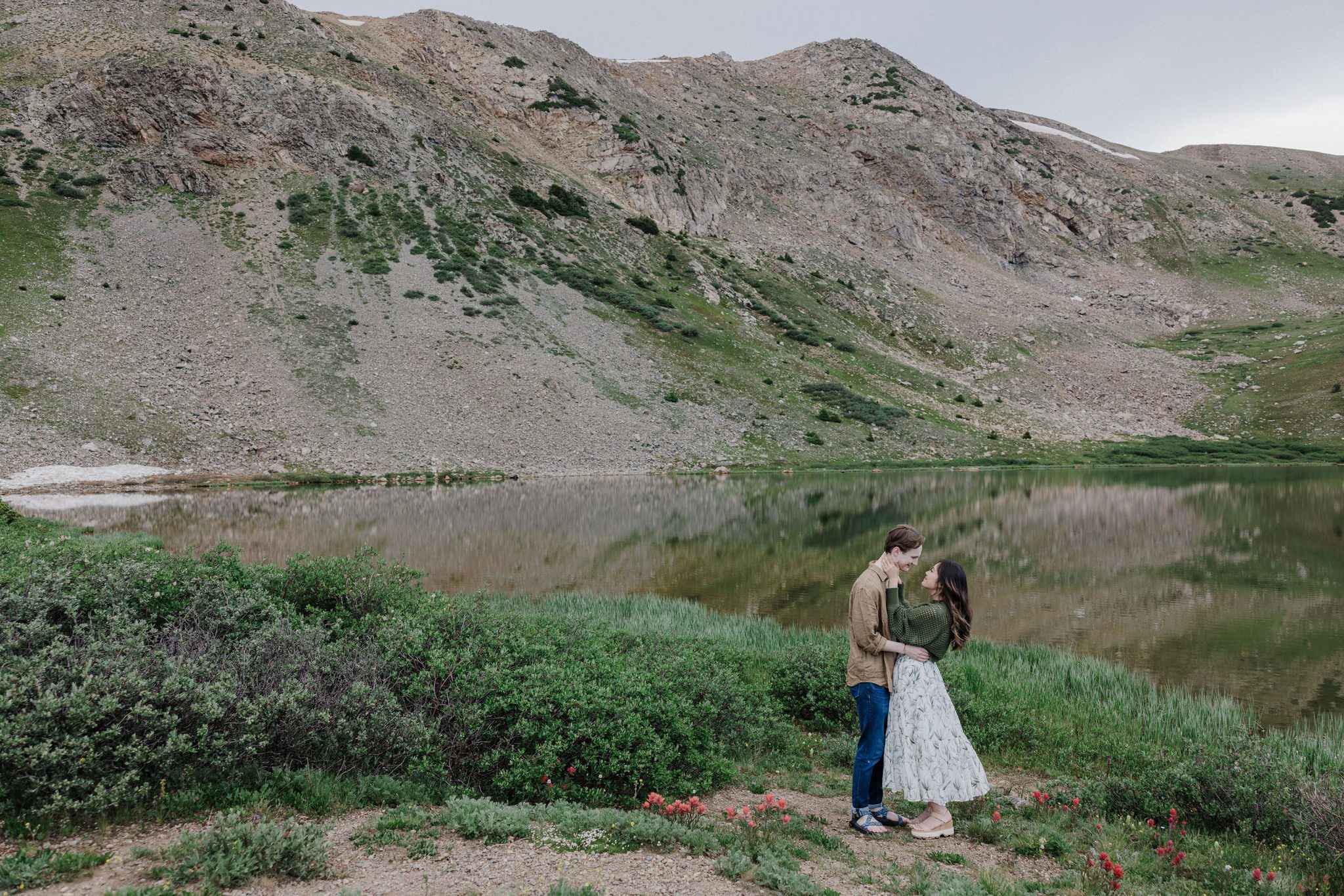 man and woman kiss beside loveland pass lake during engagement photo shoot