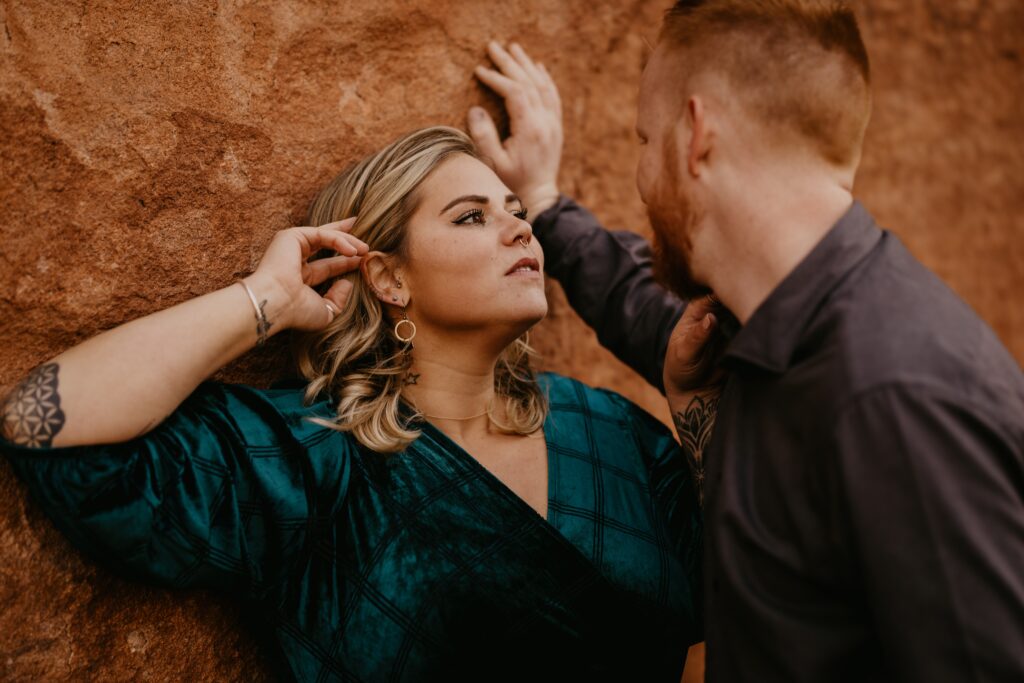 man and woman lean against red rock during colorado engagement photos.
