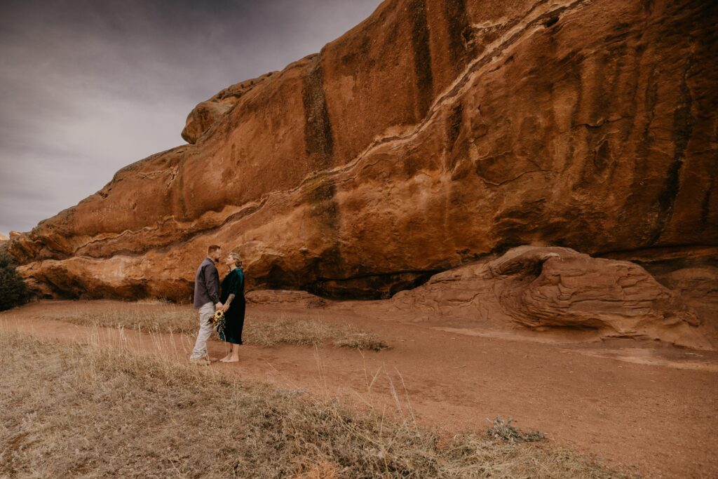 man and woman stand in front of red rocks during colorado engagement photos.