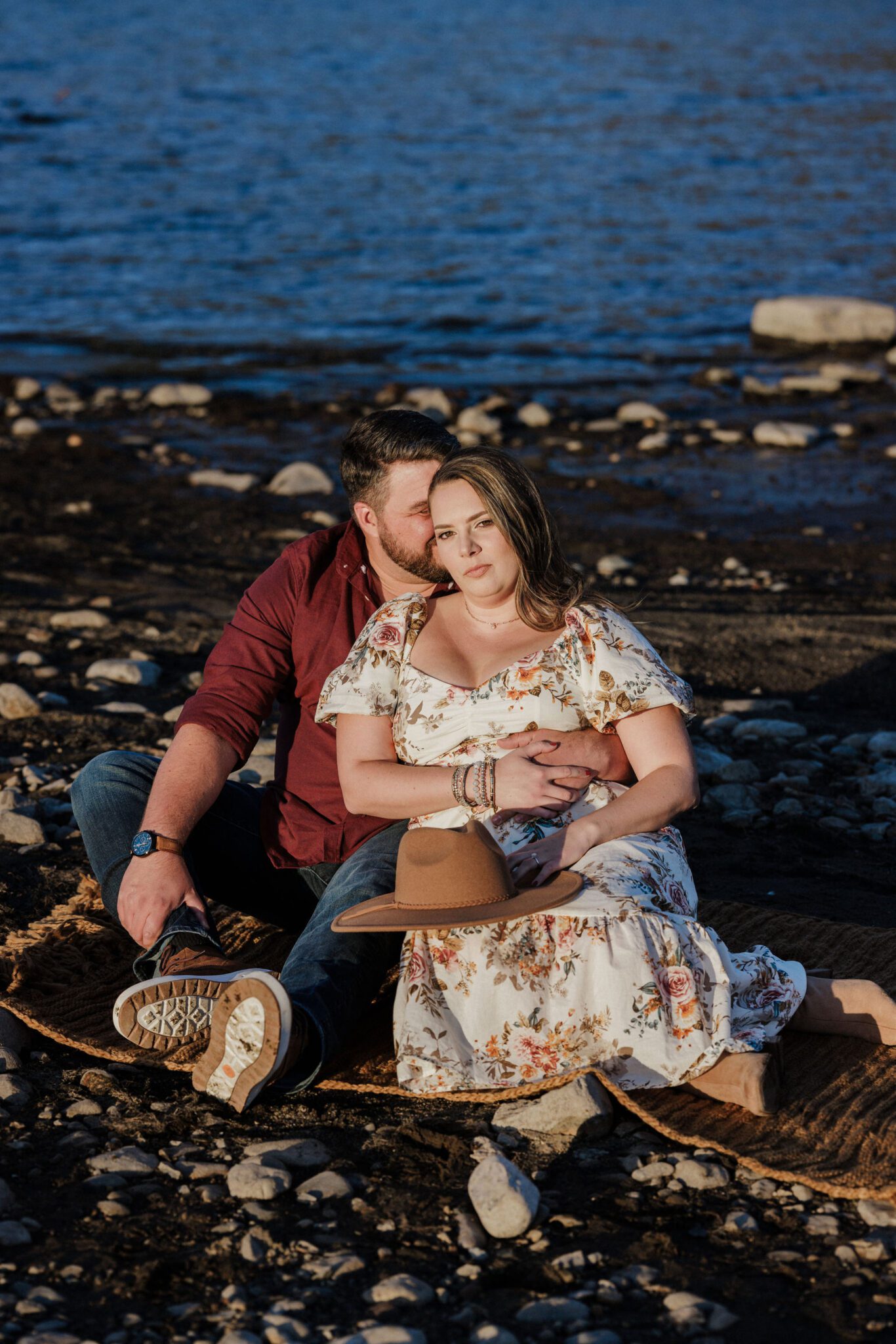 man and woman sit by edge of lake during colorado engagement photos