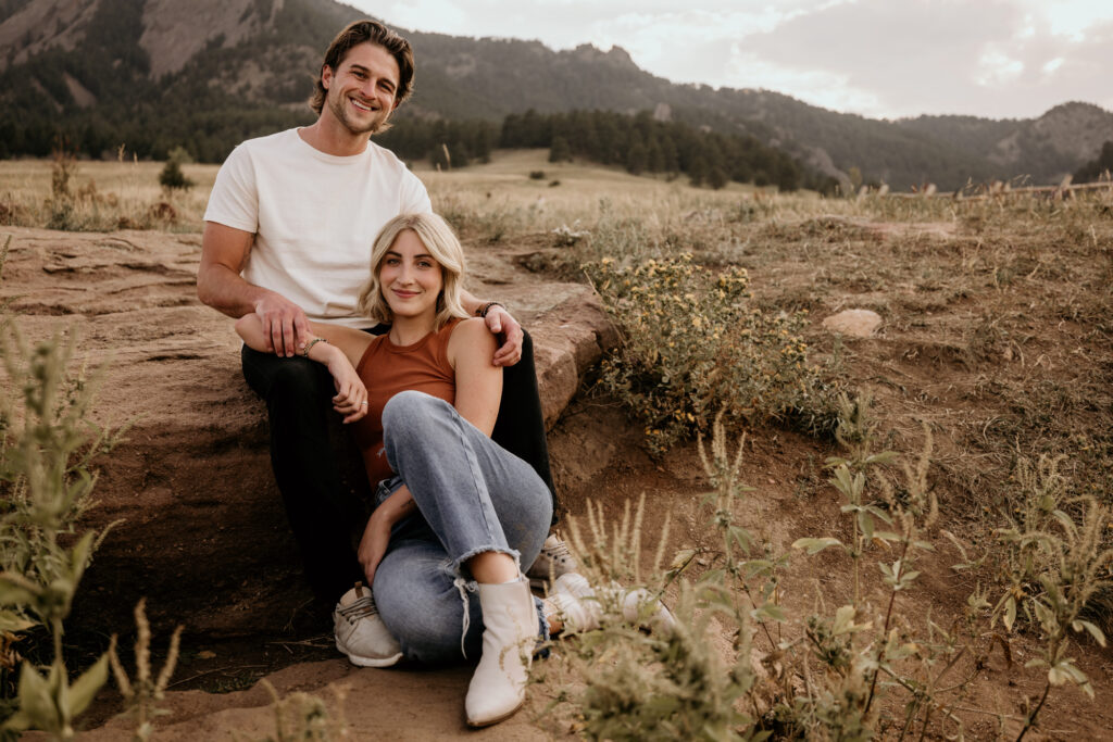 man and woman pose sitting on a rock at colorado engagement photo location.