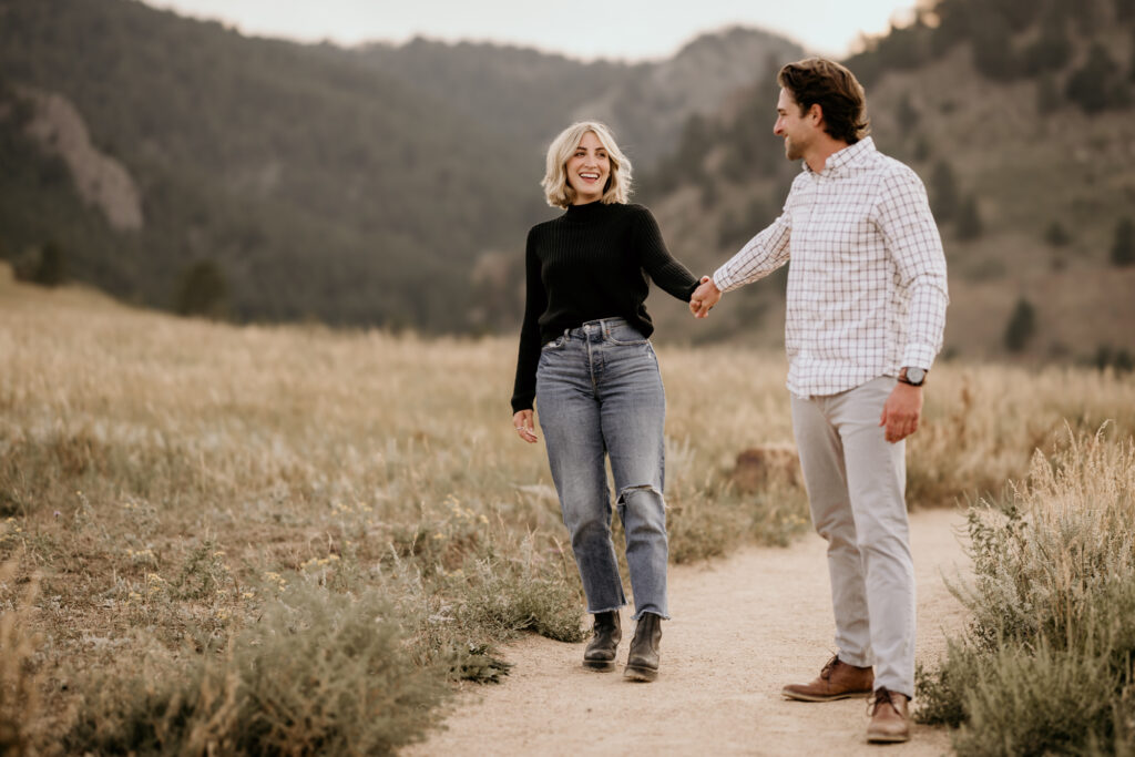 man and woman walk along trail during engagement photos in colorado.