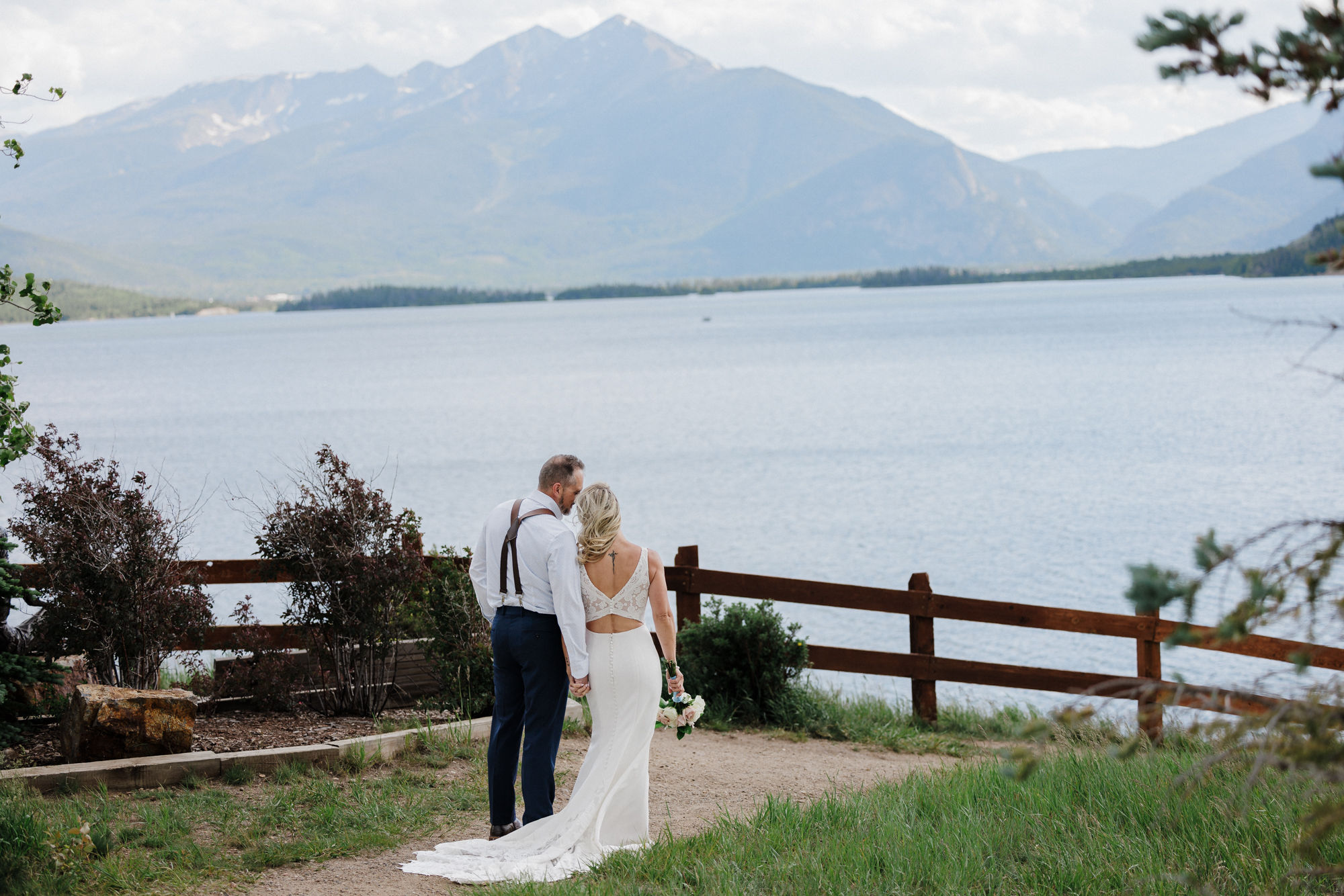 bride and groom stand in front of mountain lake during micro wedding