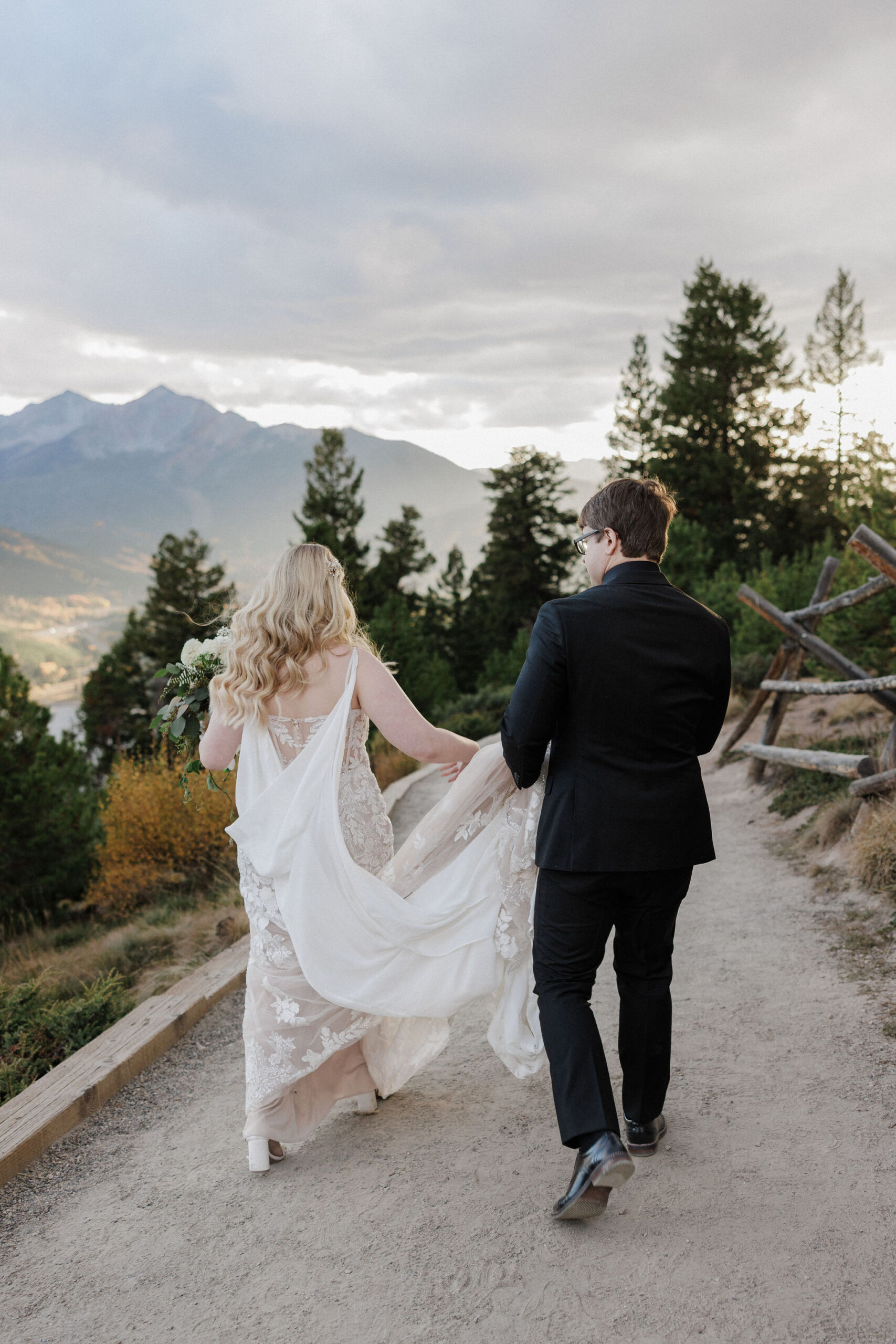 groom holds brides dress as they walk to wedding photo location