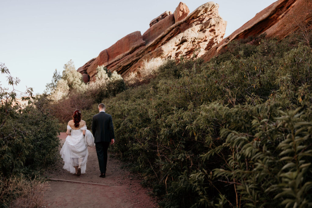 bride and groom wlak along trail at red rocks park & amphitheatre during wedding portraits.