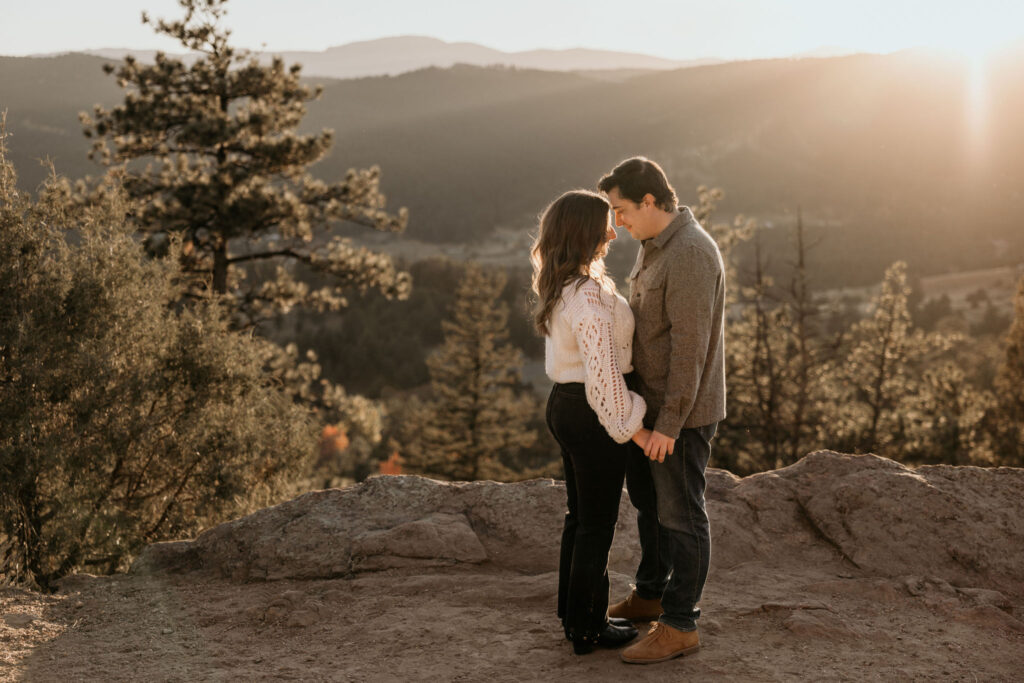 man and woman touch heads during sunset engagement photos.