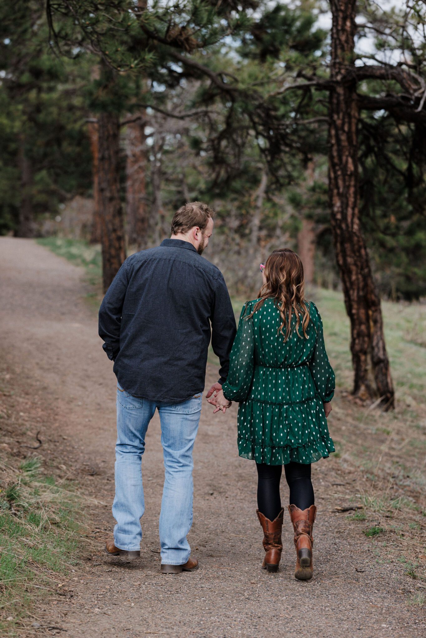 engaged couple holds hands and walk along trail during couples photo shoot