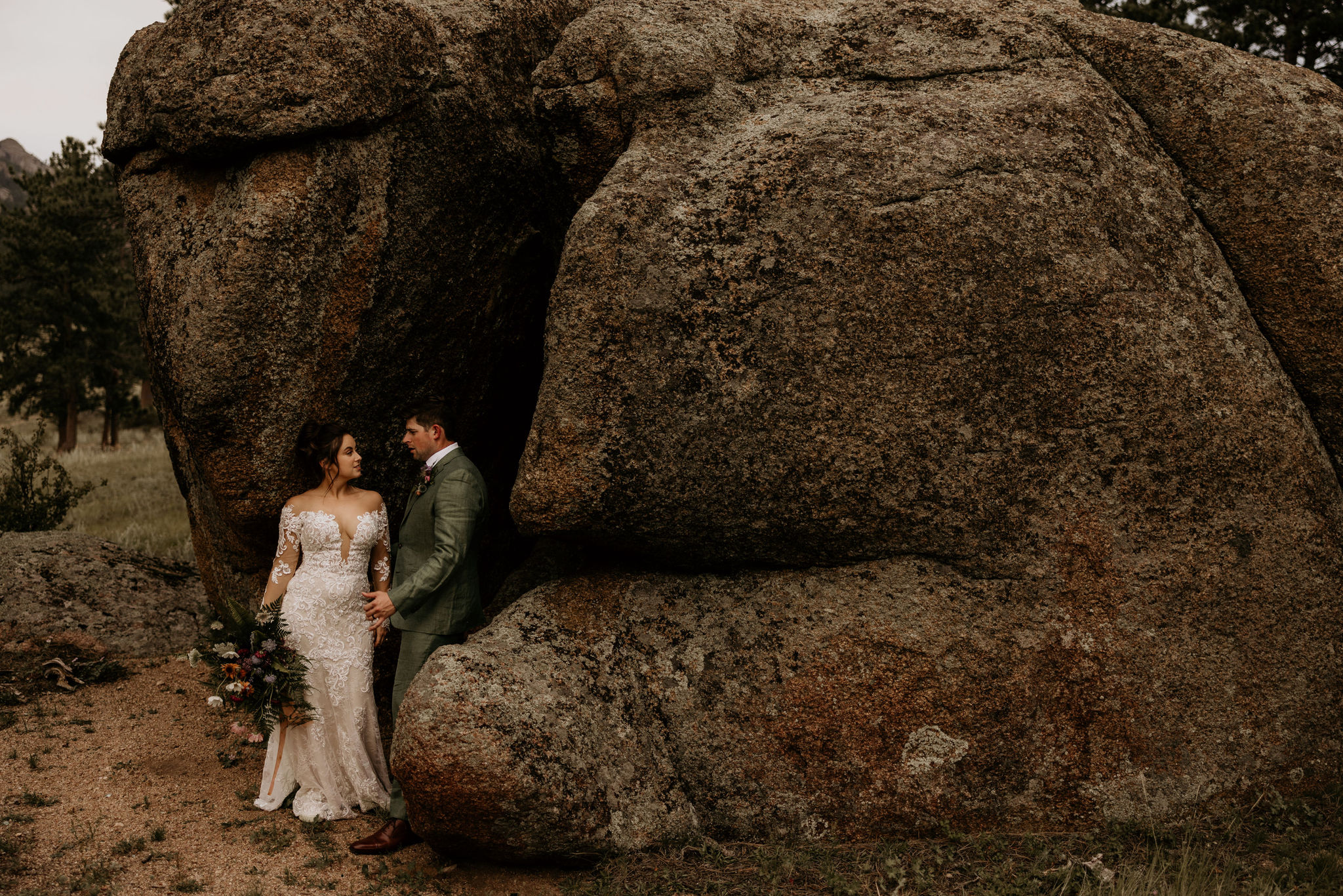 bride and groom stand against rocks during wedding photos.