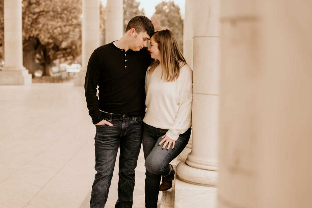 man and woman lean against column during engagement photos in denver.