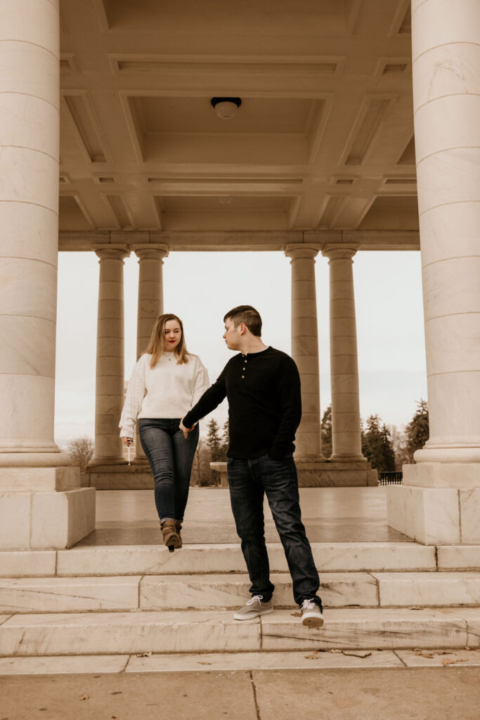 man and woman walk down marble steps during engagement photos in denver.
