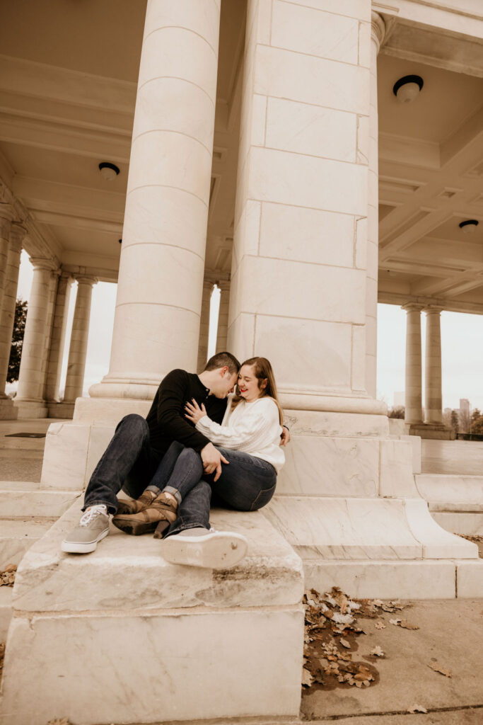 man and woman sit on marble ledge during denver engagement photos at cheesman park.