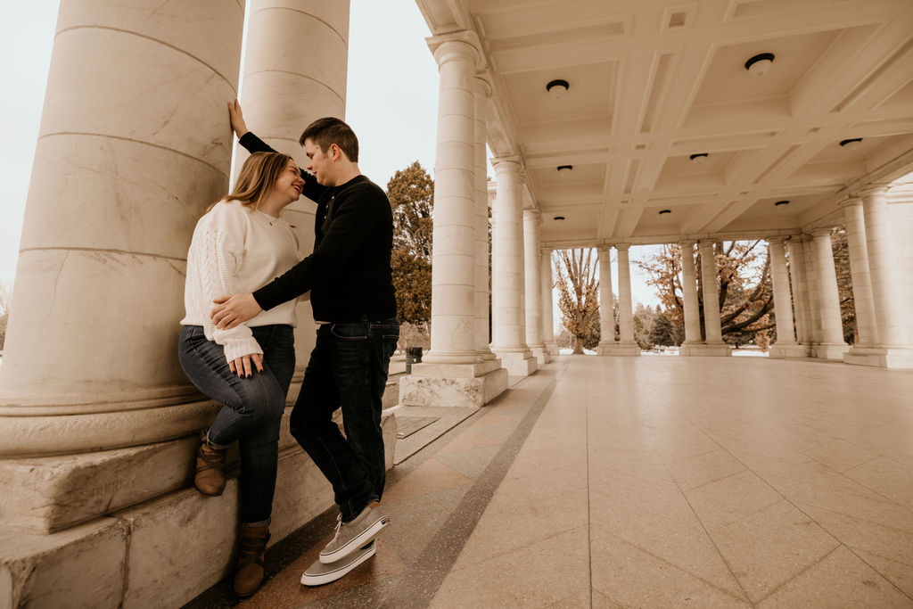 man and woman lean against marble column during engagement photos in denver.