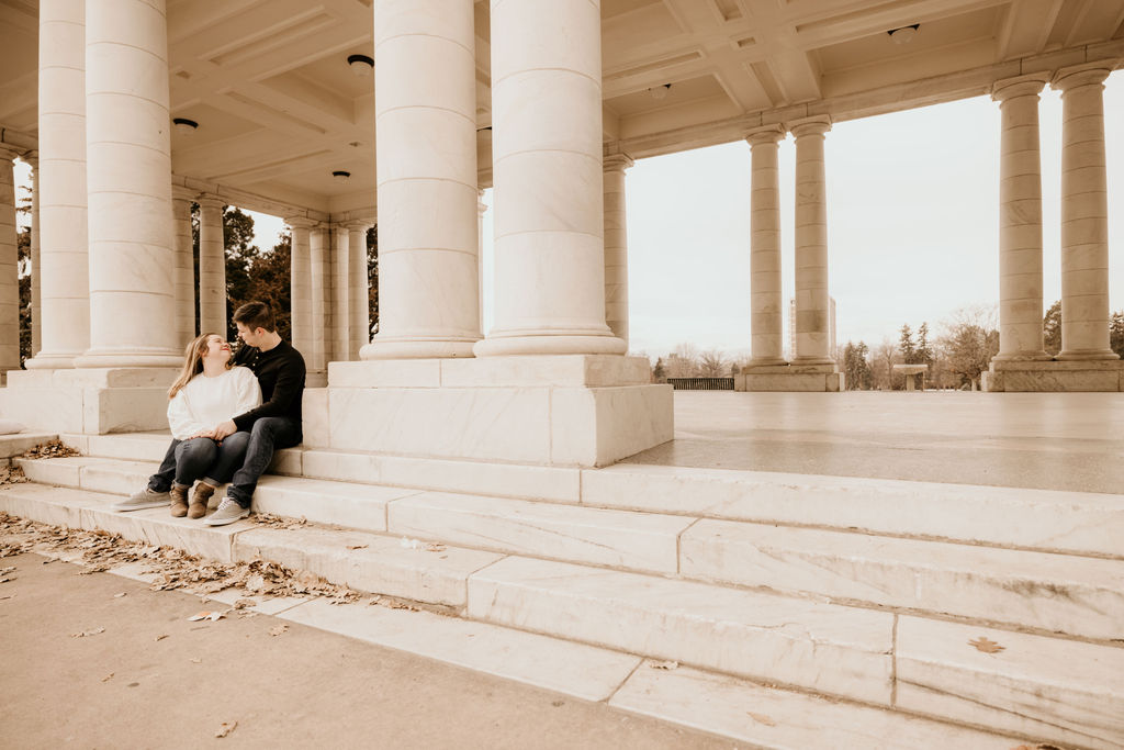 man and woman sit on marble steps during denver engagement photos.