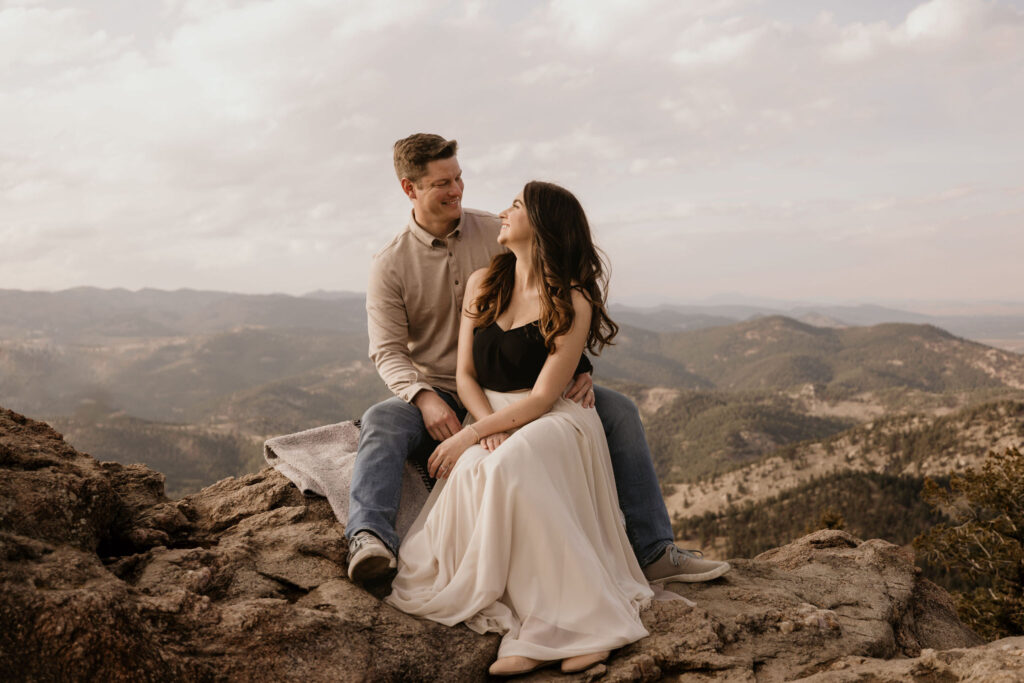 woman and man sit on rock ledge at lost gulch during engagement photos.