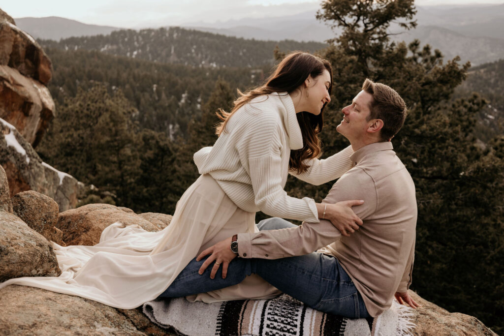 man and woman sit on rock ledge during colorado engagement photos at lost gulch.