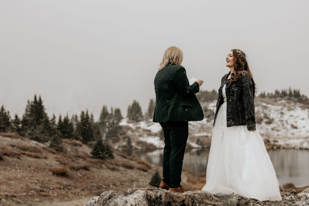 LGBTQ+ couple stands on rock in the snow during colorado couples portraits.