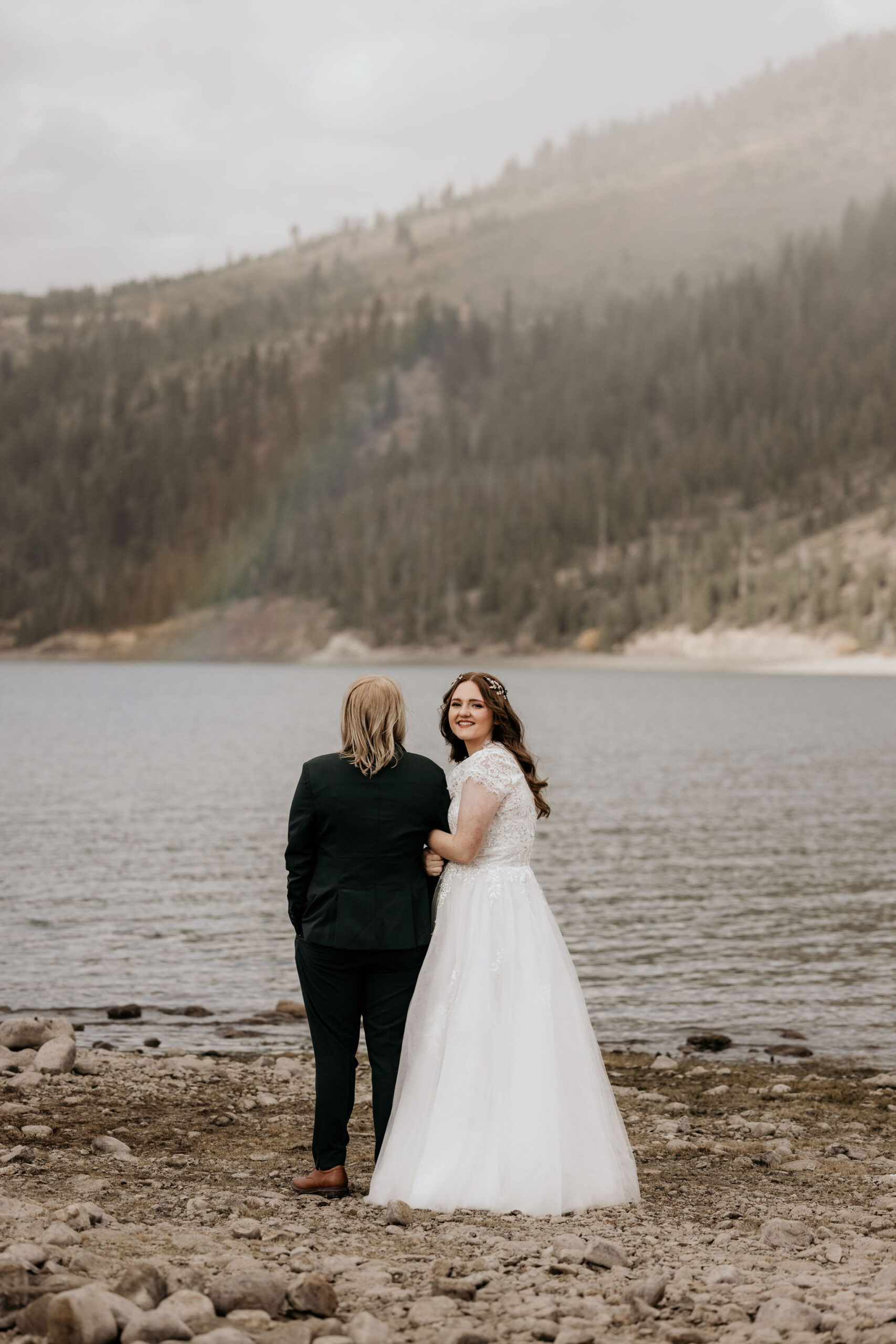 LGBTQ+ stands on shore of dillon reservoir during couples photos in colorado.