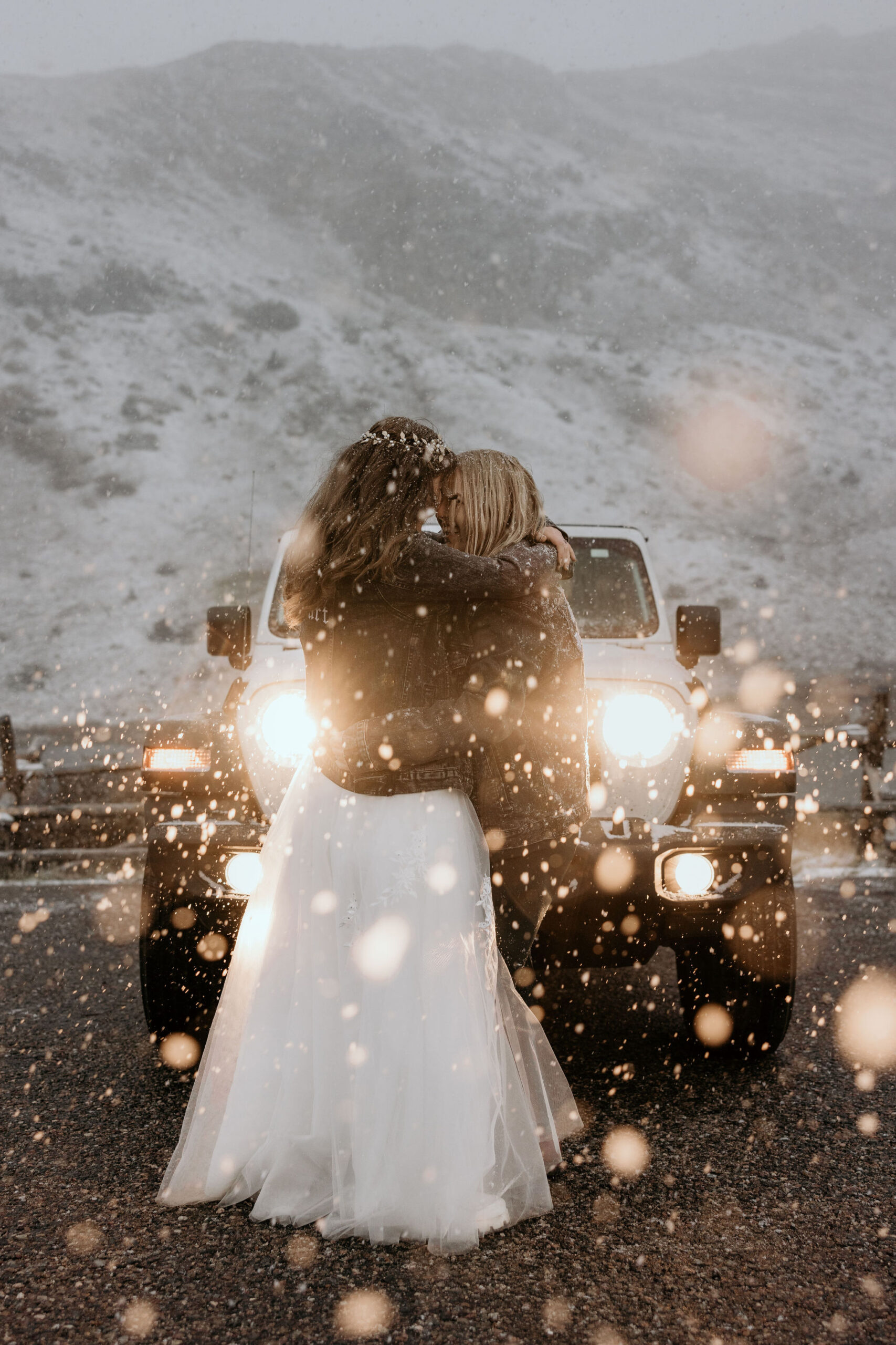 LGBTQ+ couple hugs in front of jeep in the snow during stress-free wedding.