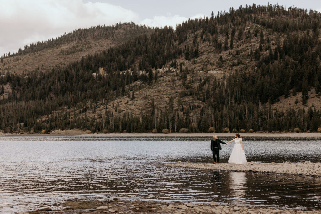 lgbtq+ couple hold hands at the edge of colorado lake during mountain elopement.