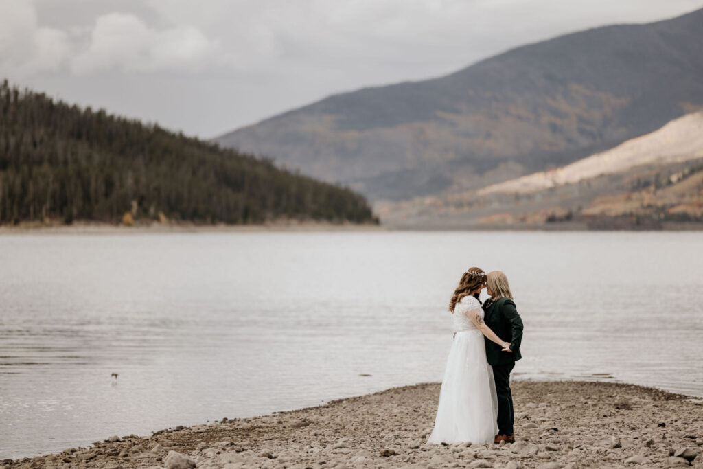 lgbtq+ couple embraces on the edge of alpine lake for colorado elopement.