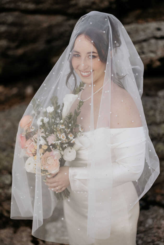 bride holds wedding bouquet and smiles under wedding veil.