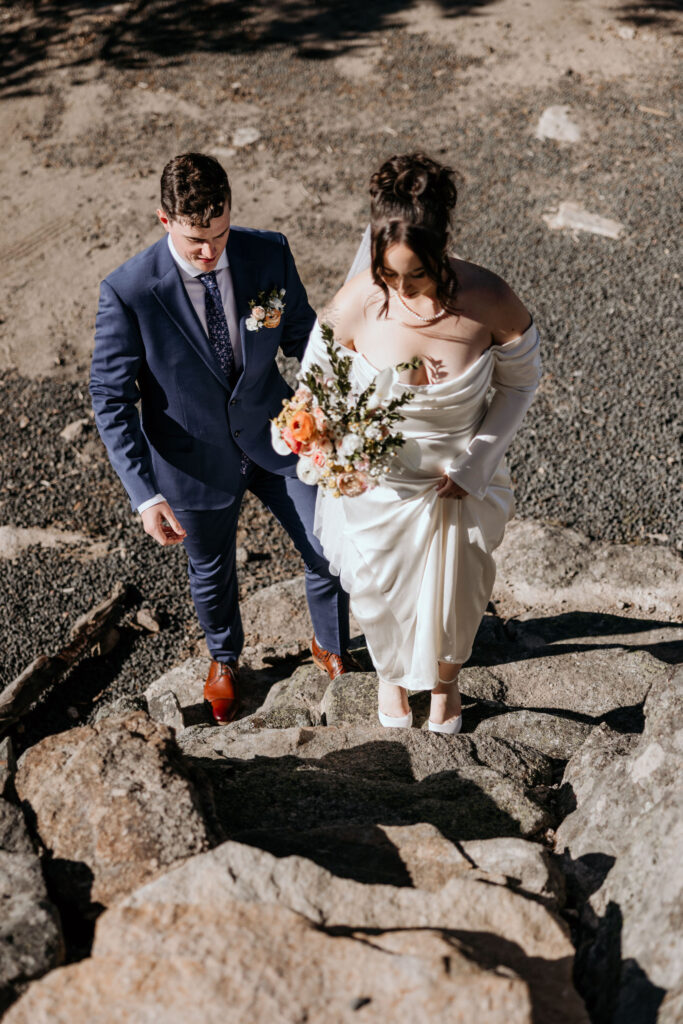 bride and groom walk up rock steps on rock formation in the colorado mountains.