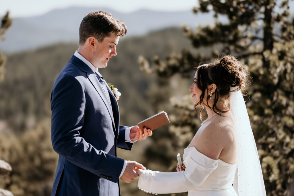 groom holds brides hand and reads wedding vows during elopement ceremony.
