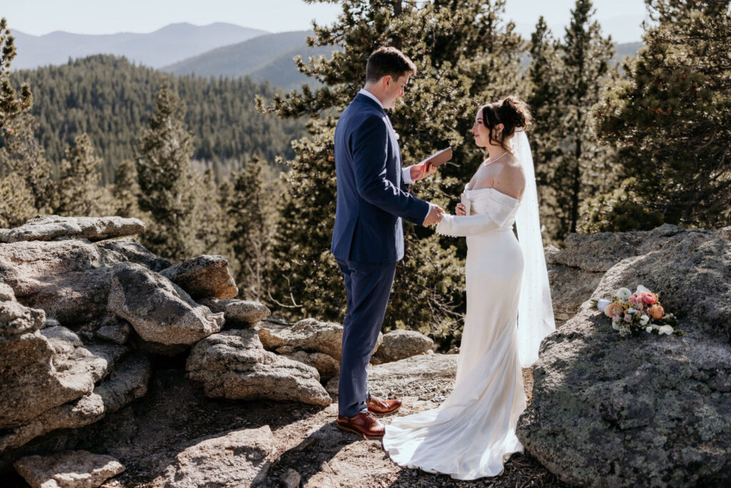 man and woman read wedding vows in front of the colorado mountains.