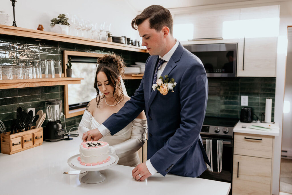 bride and groom cut vintage style wedding cake in colorado airbnb kitchen.