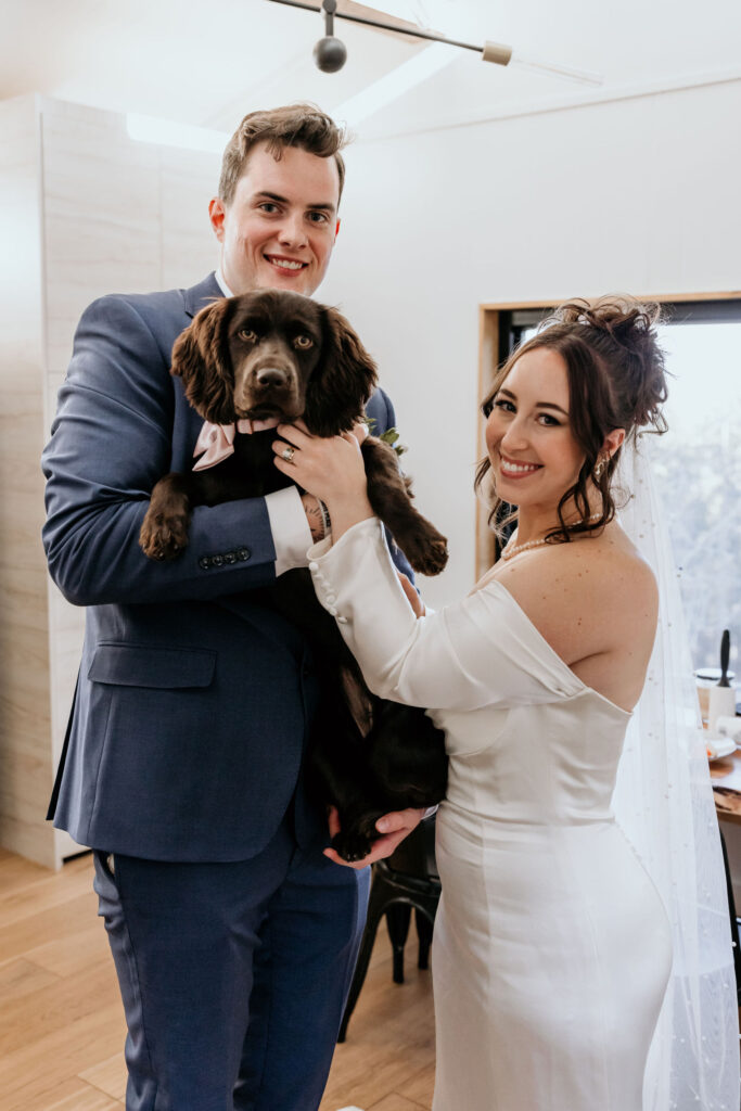 bride and groom hold up little brown dog during airbnb elopement in colorado.