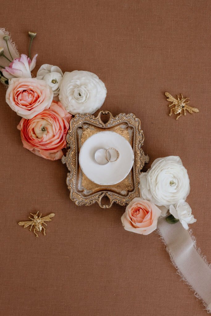 flat lay photo of wedding bands on a small gold tray and flowers.