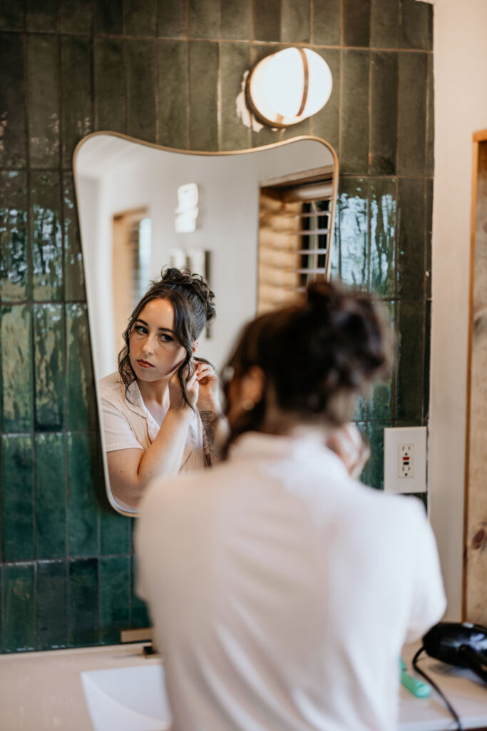 bride puts earrings in while looking in mirror during colorado airbnb elopement.
