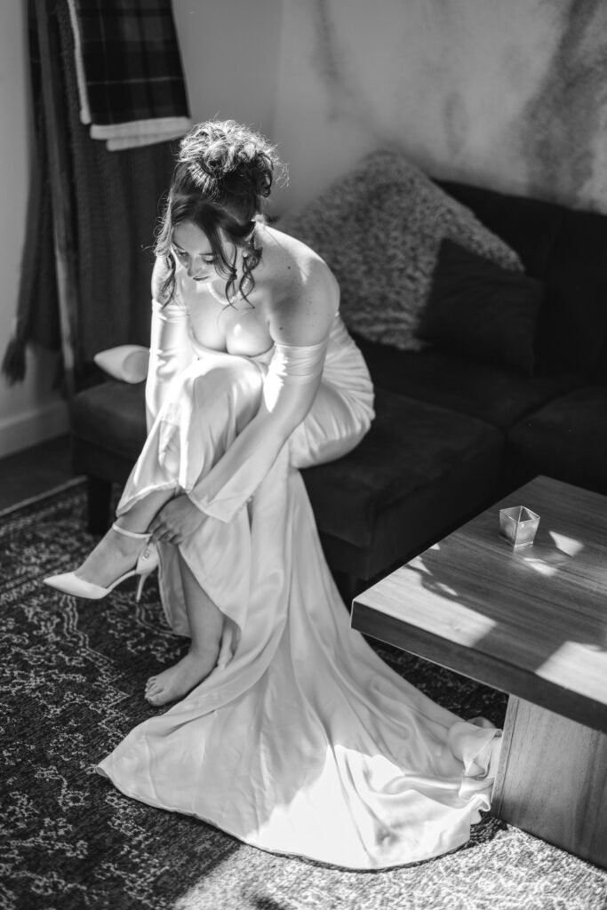 bride sits on couch and puts wedding shoes on.