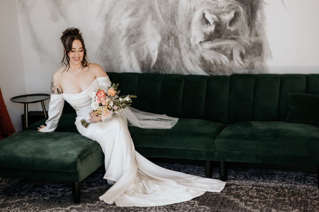 bride smiles and sits on green couch during elopement bridal portraits.