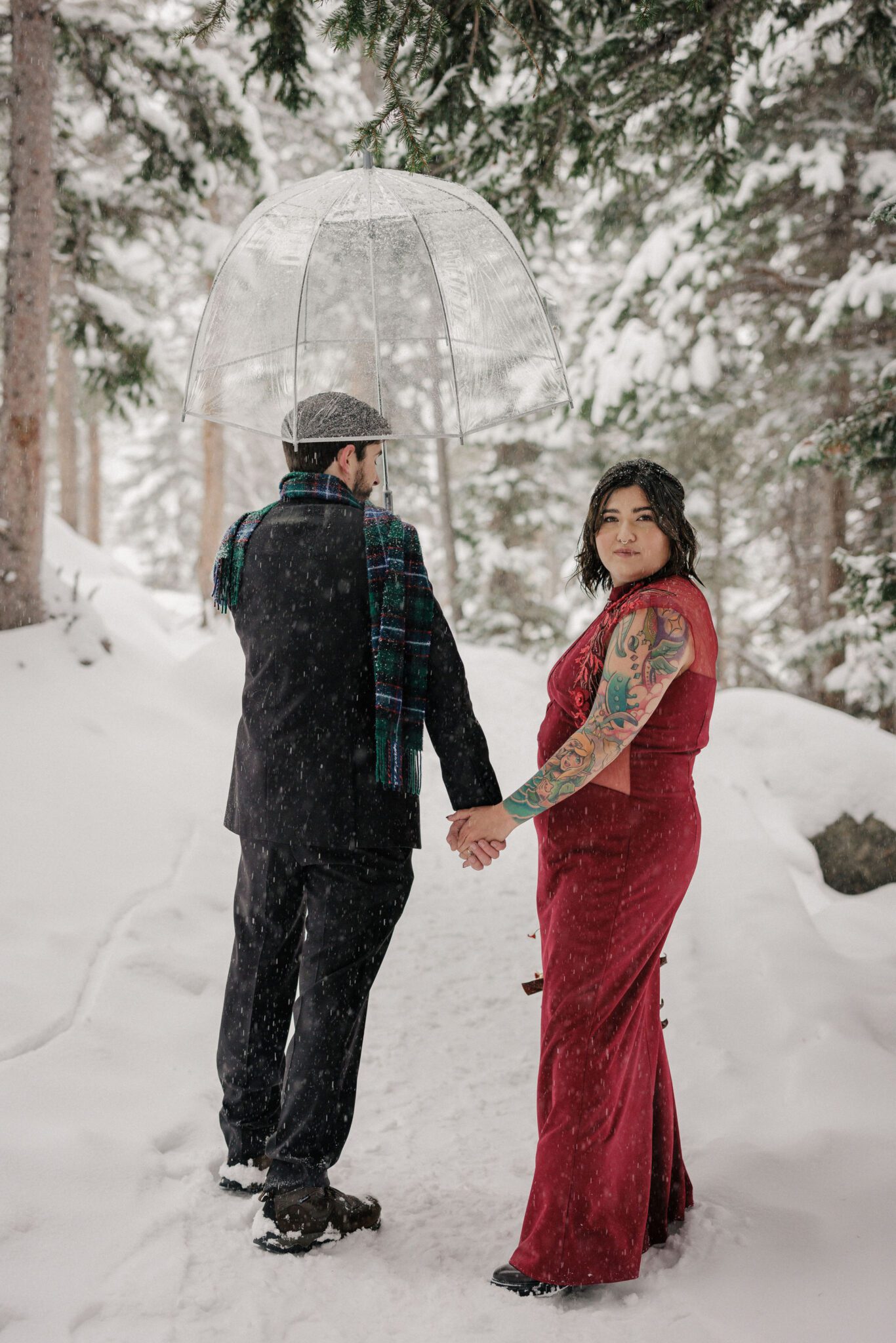 man and woman hold hands and walk through snow during colorado couples photo shoot