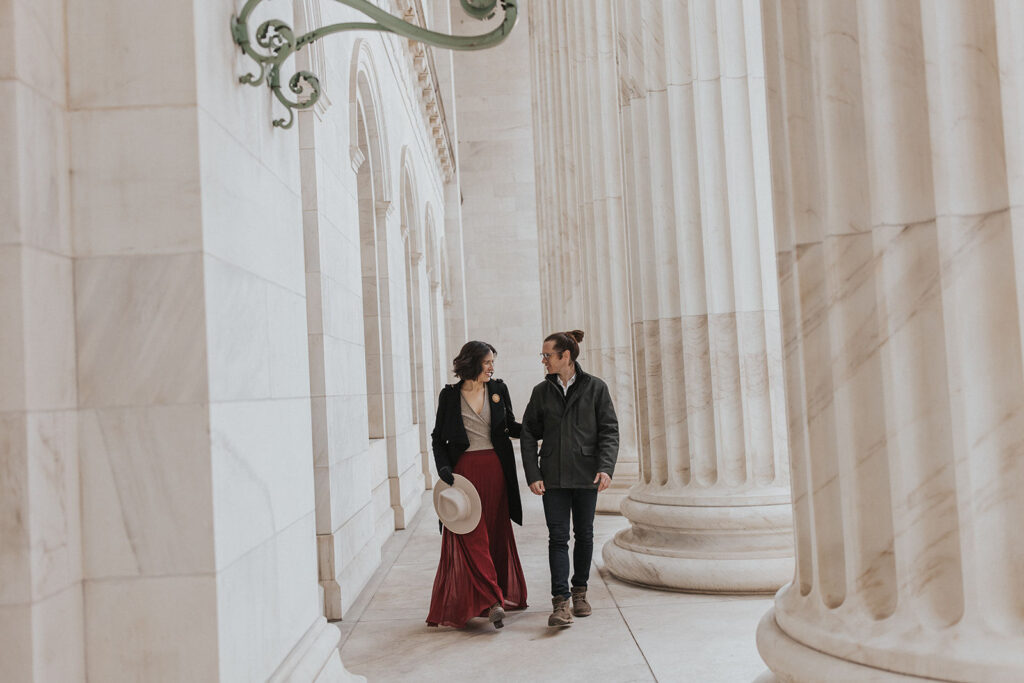 man and woman walk down marble walkway during denver engagement photos.