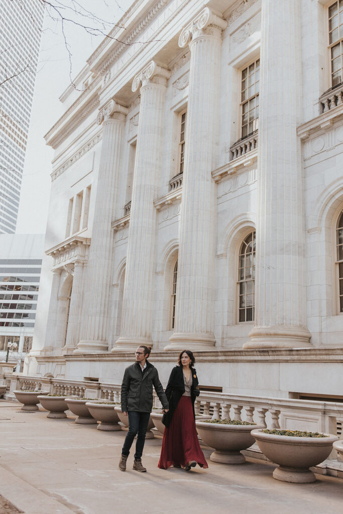 man and woman walk along byron white courthouse during couples portraits.