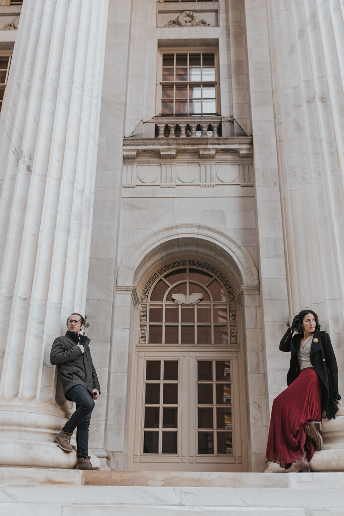 man and woman lean again marble columns during downtown denver engagement photo shoot.