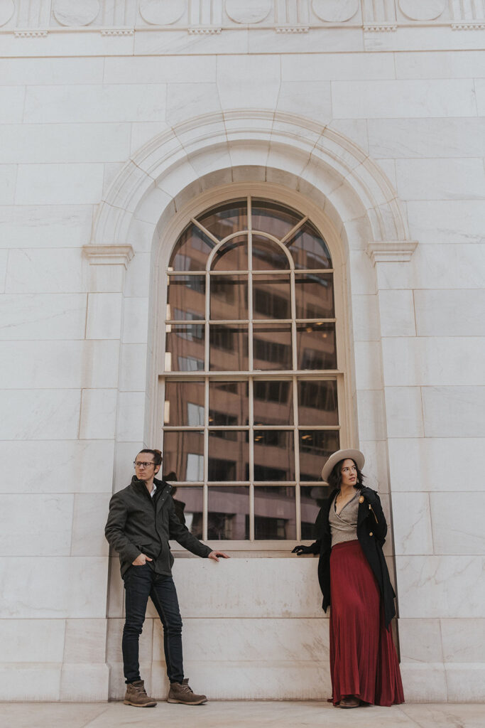 man and woman stand in front of window during denver engagement photos.