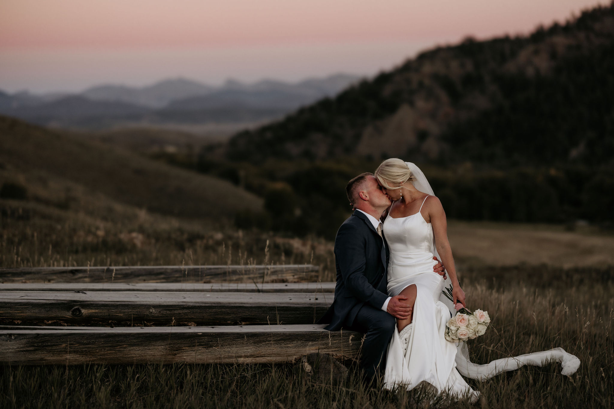 bride sits on grooms lap on a bench in the colorado mountains.