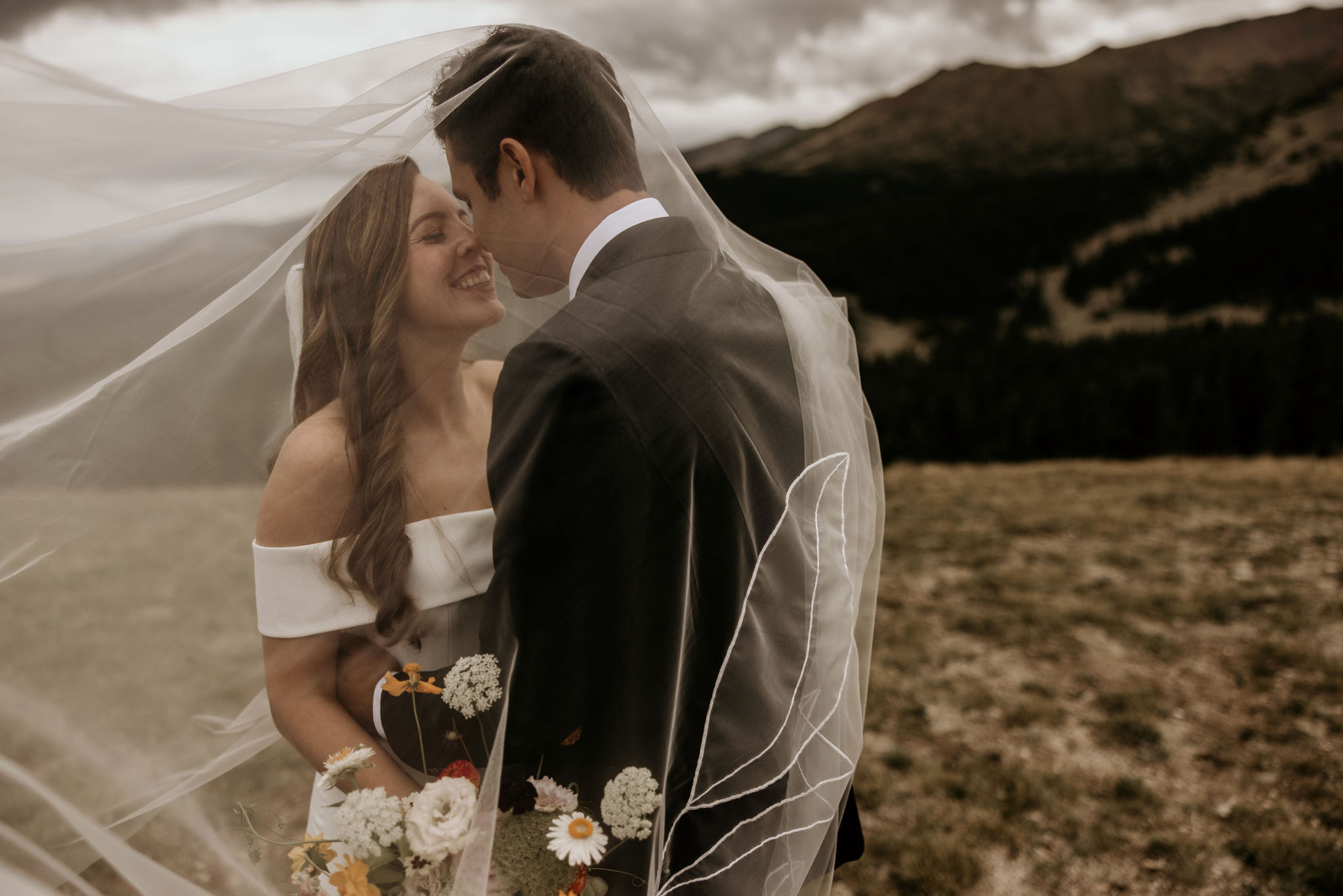 bride and groom smile under veil during colorado elopement.