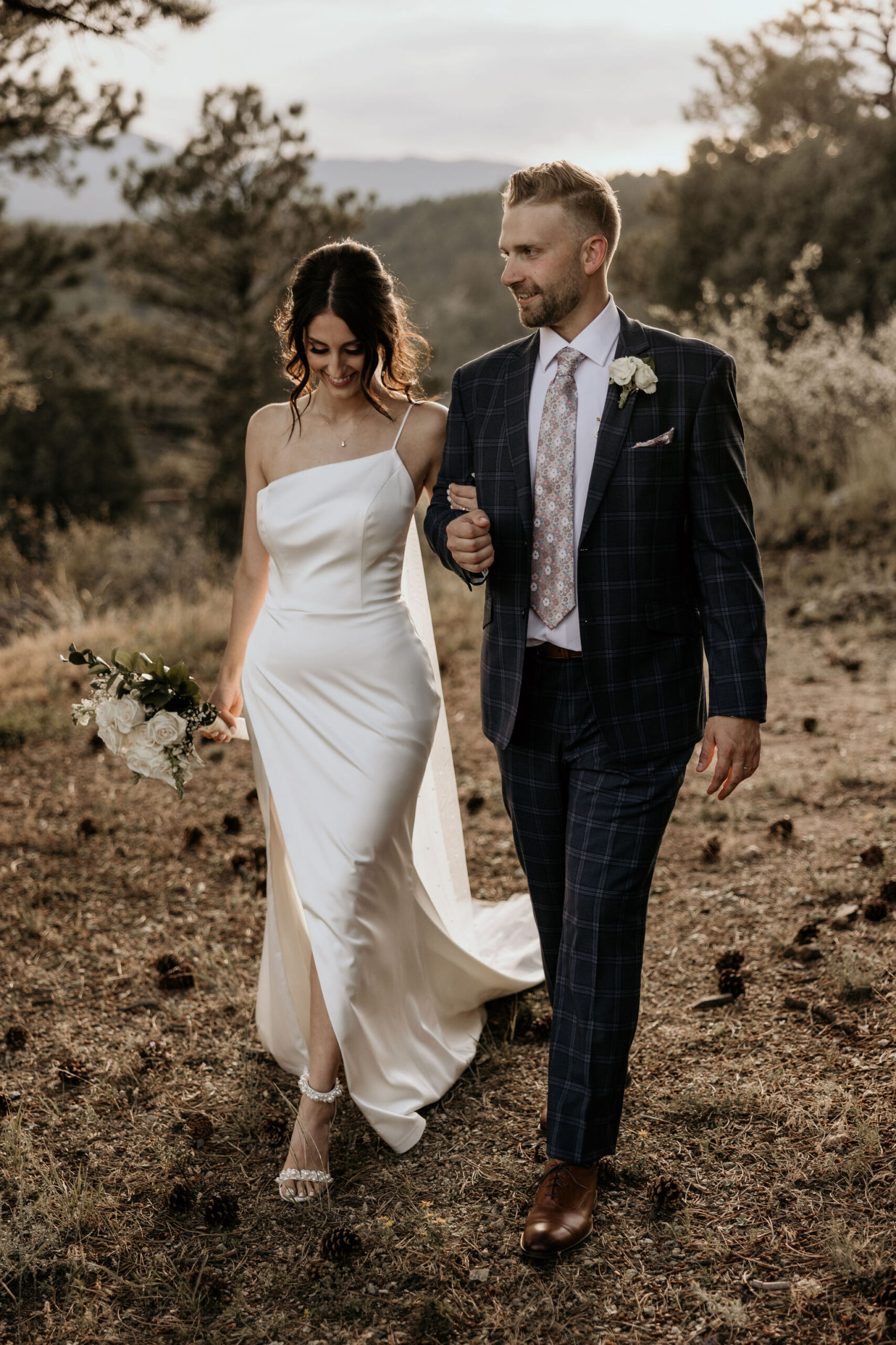 bride and groom walk arm in arm in the colorado mountains.