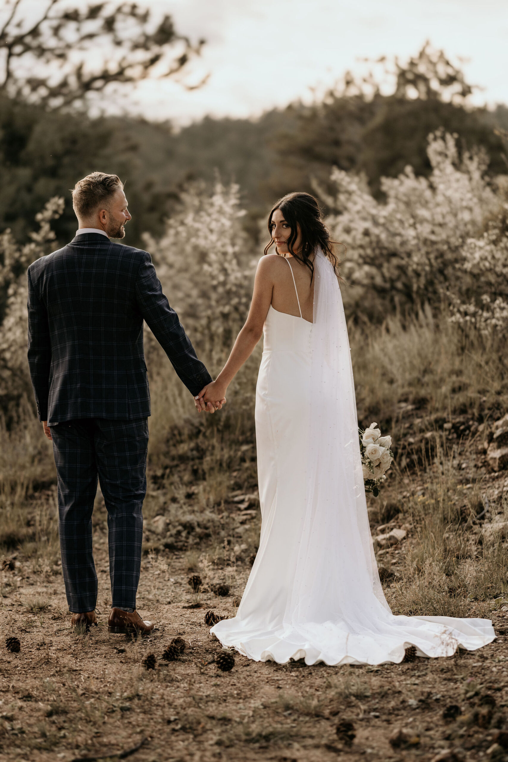 bride and groom hold hands and walk on trail during colorado elopement.